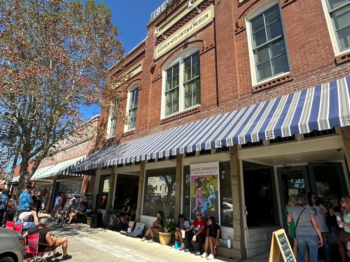 Shops with blue-and-white awnings on a sunny street, with people browsing and sitting outside.