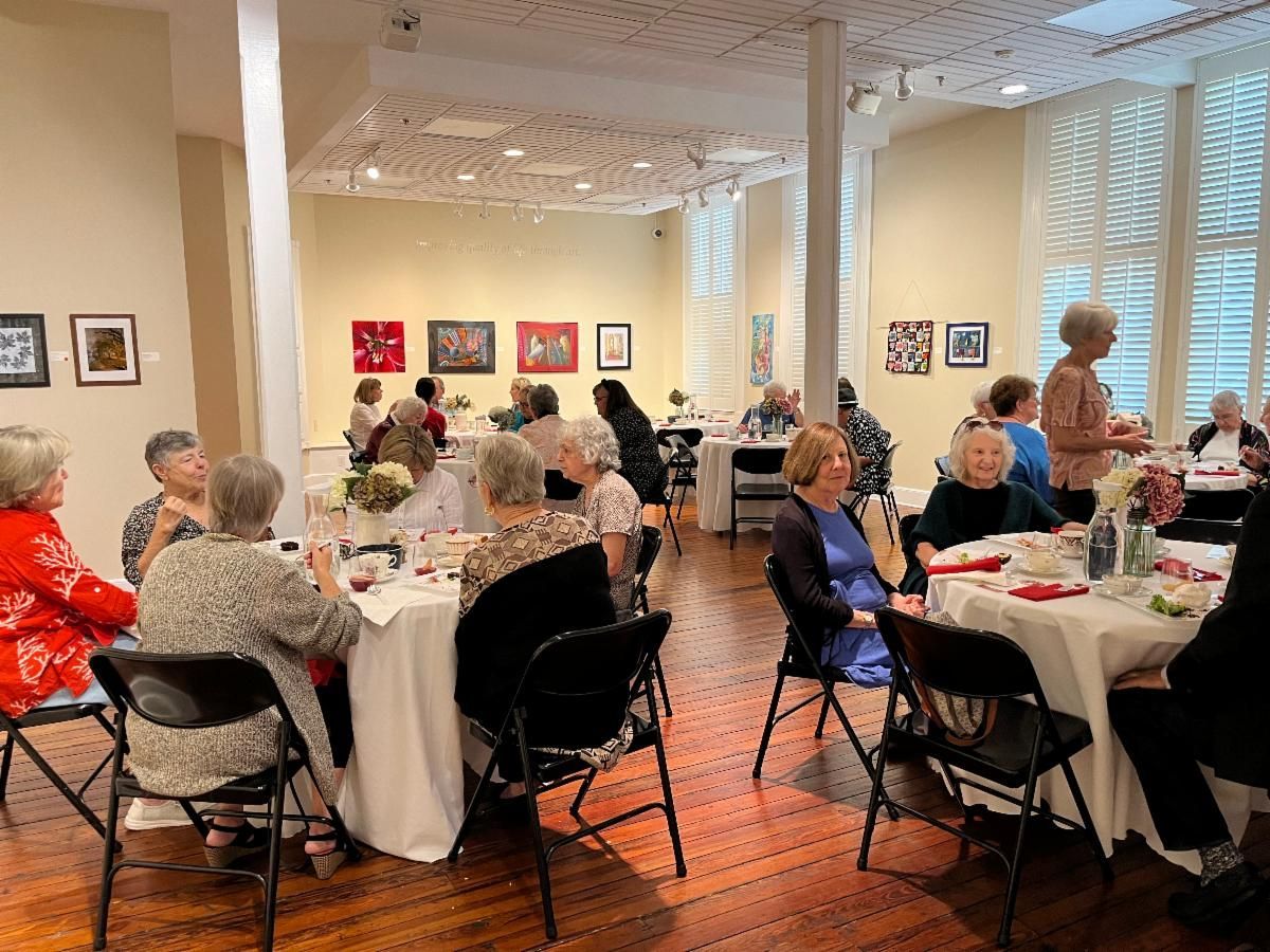 Guests seated at round tables in a bright art gallery, conversing during a social event