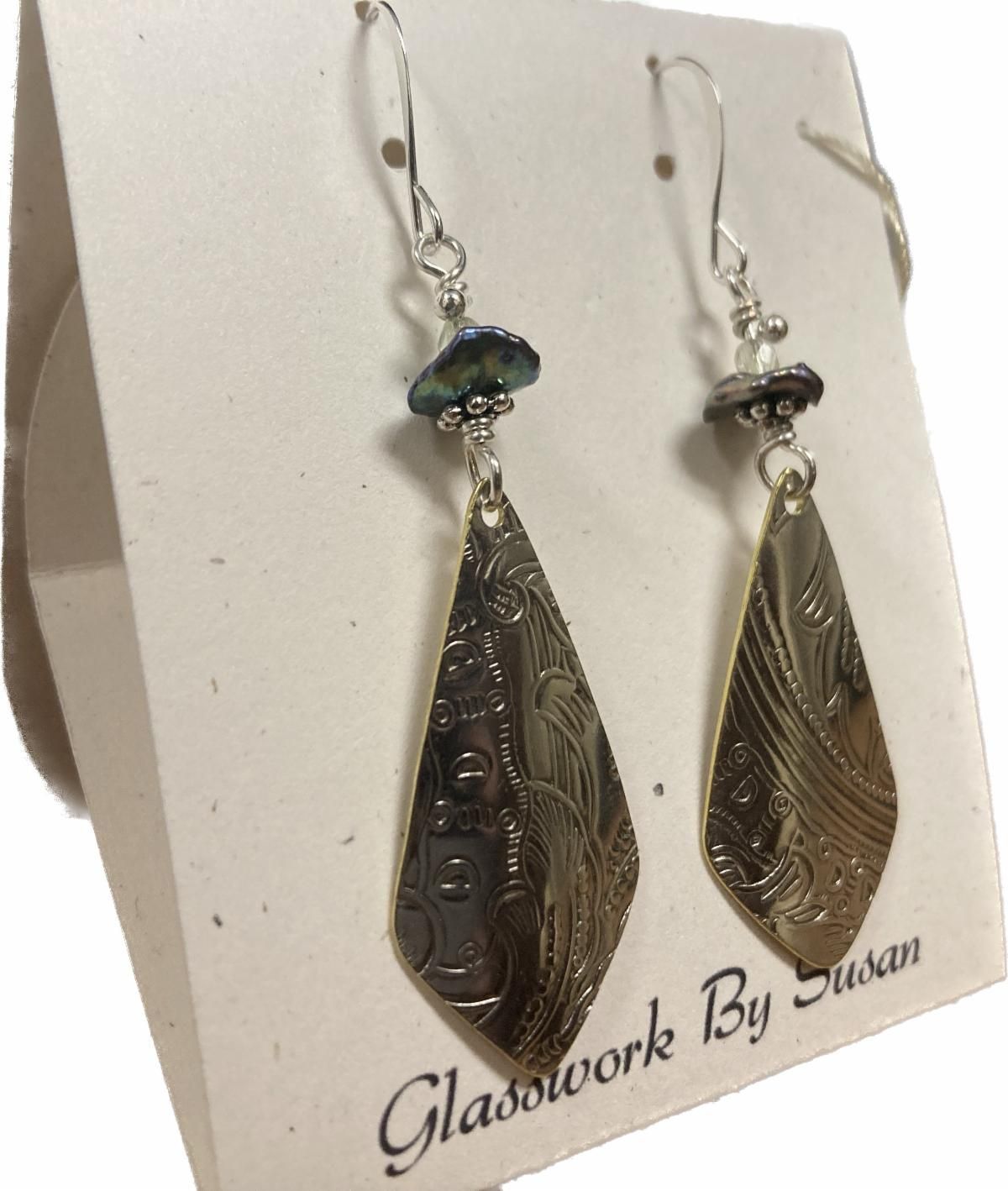 Pair of dangling silver-toned earrings with etched teardrop pendants and iridescent beads on a display card