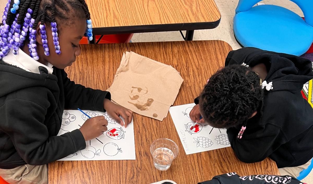 Two children painting at a table with paper, brushes, and a cup of water