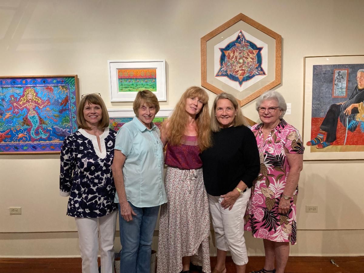 Five women posing in an art gallery with colorful framed artwork on the wall