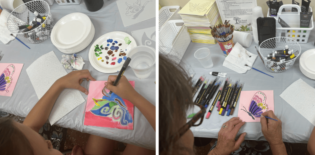 Hands painting colorful cards on a craft table with brushes, markers, paint, and paper supplies