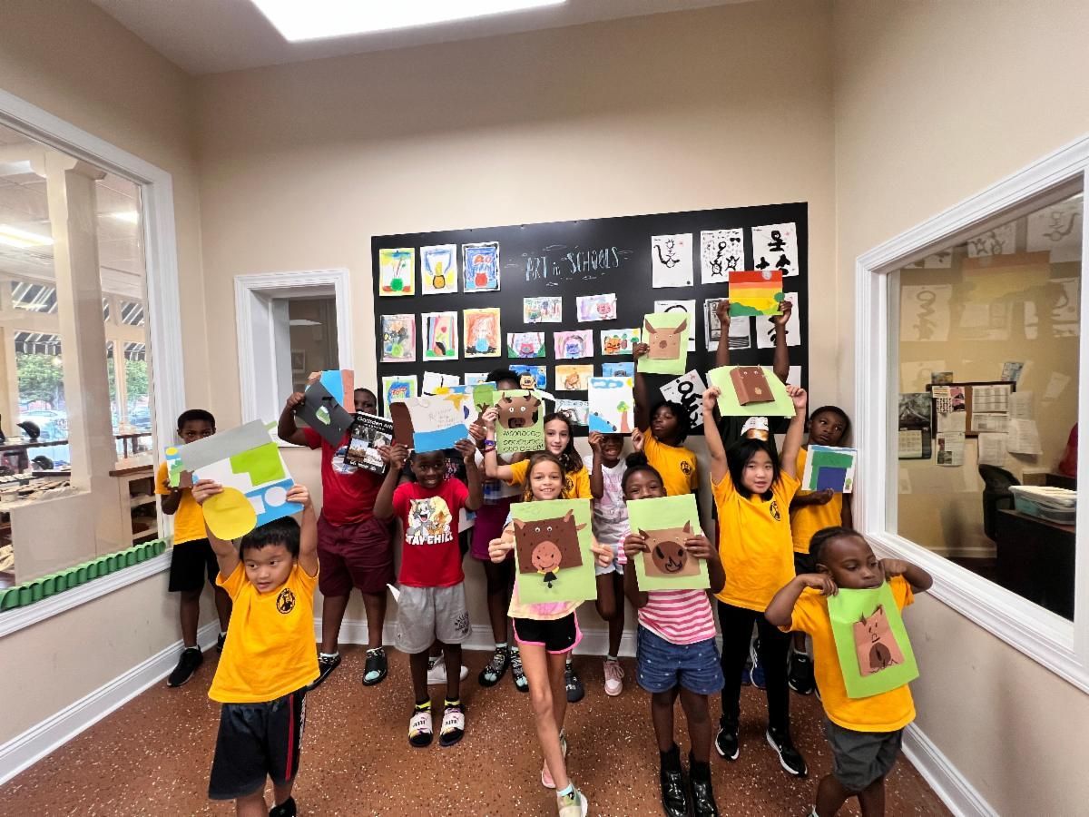 Children holding up colorful artwork in a classroom with a black display board and large windows