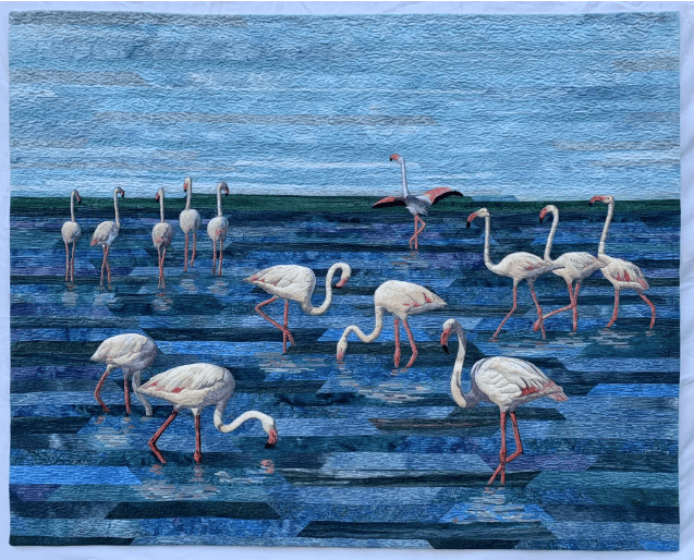 Flamingos wade and feed in shallow blue water beneath a wide sky.
