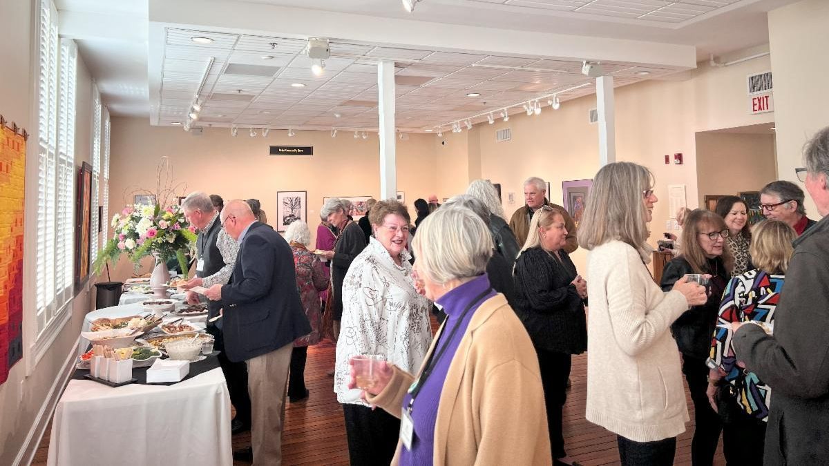 Guests mingle at a bright indoor reception with a buffet table and drinks along the wall.