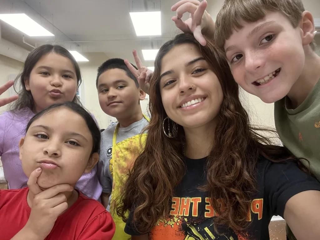 Five smiling students taking a selfie in a bright classroom