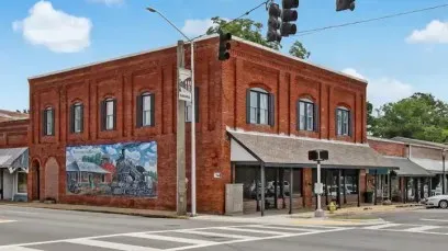 Red brick corner storefront with mural, awnings, and traffic lights at an intersection