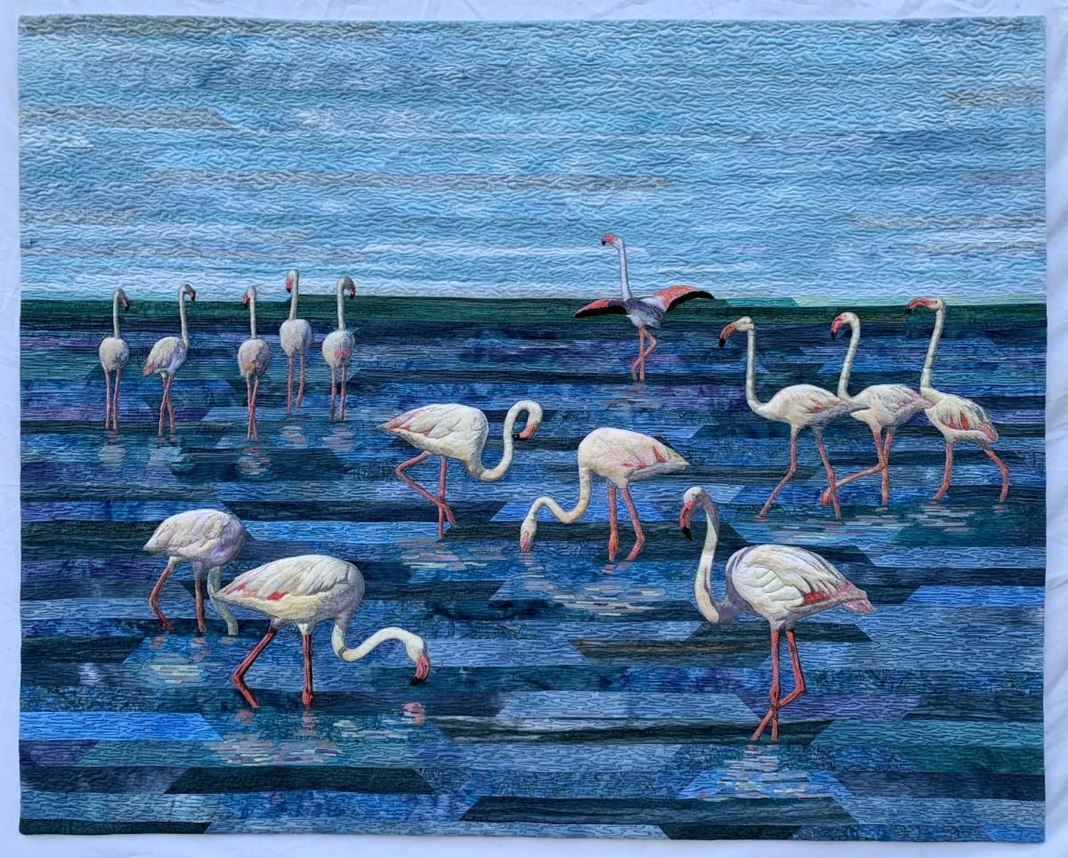 Flamingos wade and feed in blue rippling water under a cloudy sky.
