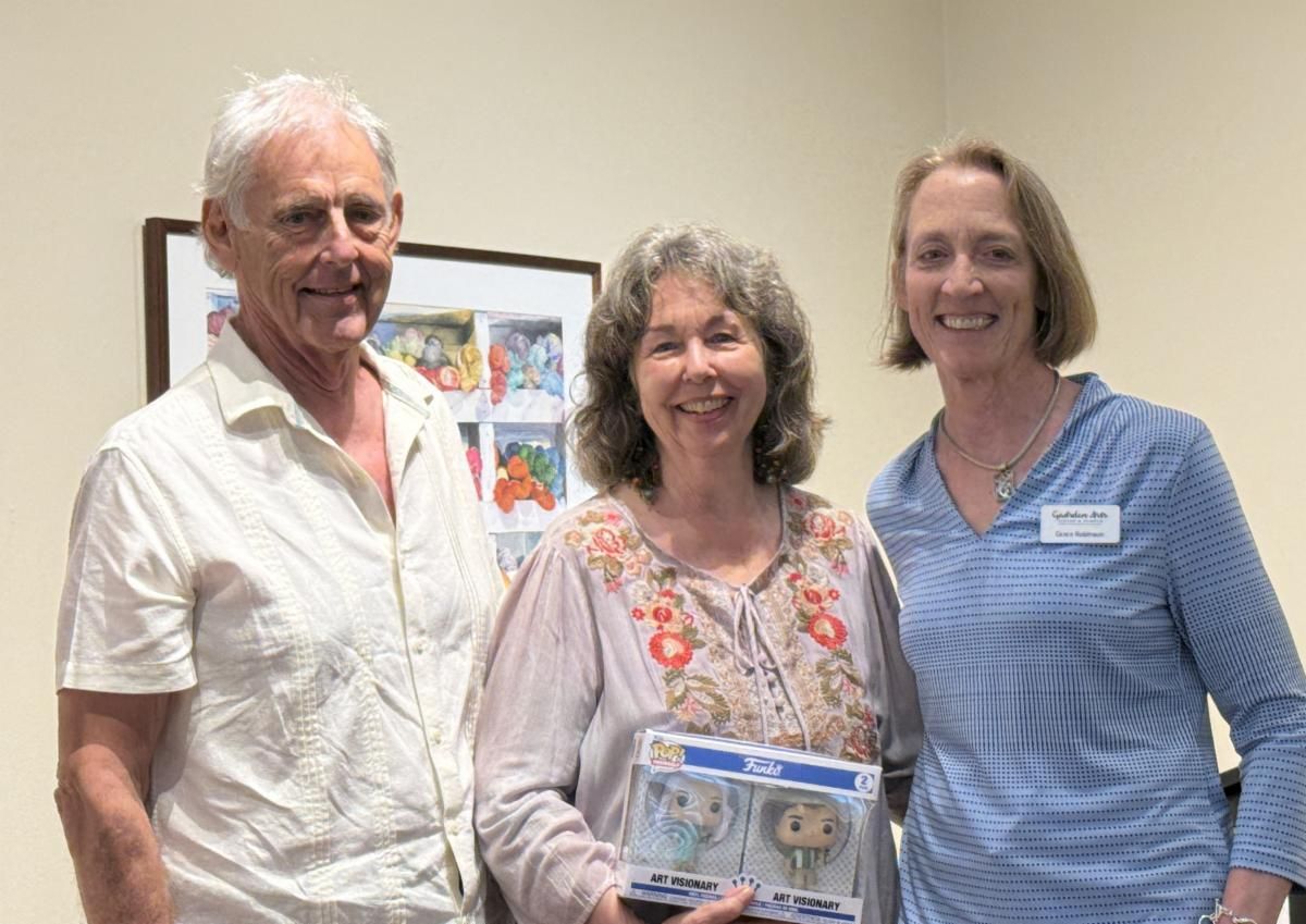 Three people smiling indoors, holding a framed award or plaque.