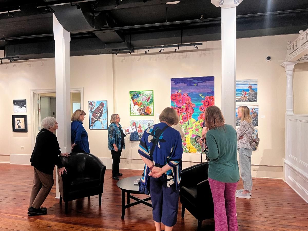 People viewing colorful paintings in an art gallery with white walls and wooden floors