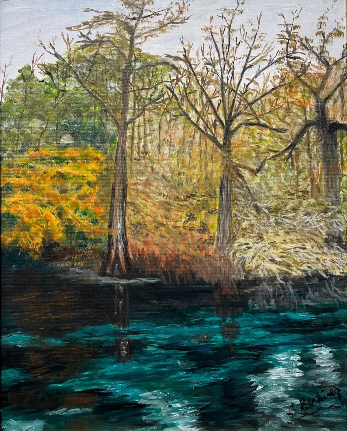 Autumn trees and shrubs beside dark teal water in a natural riverside landscape