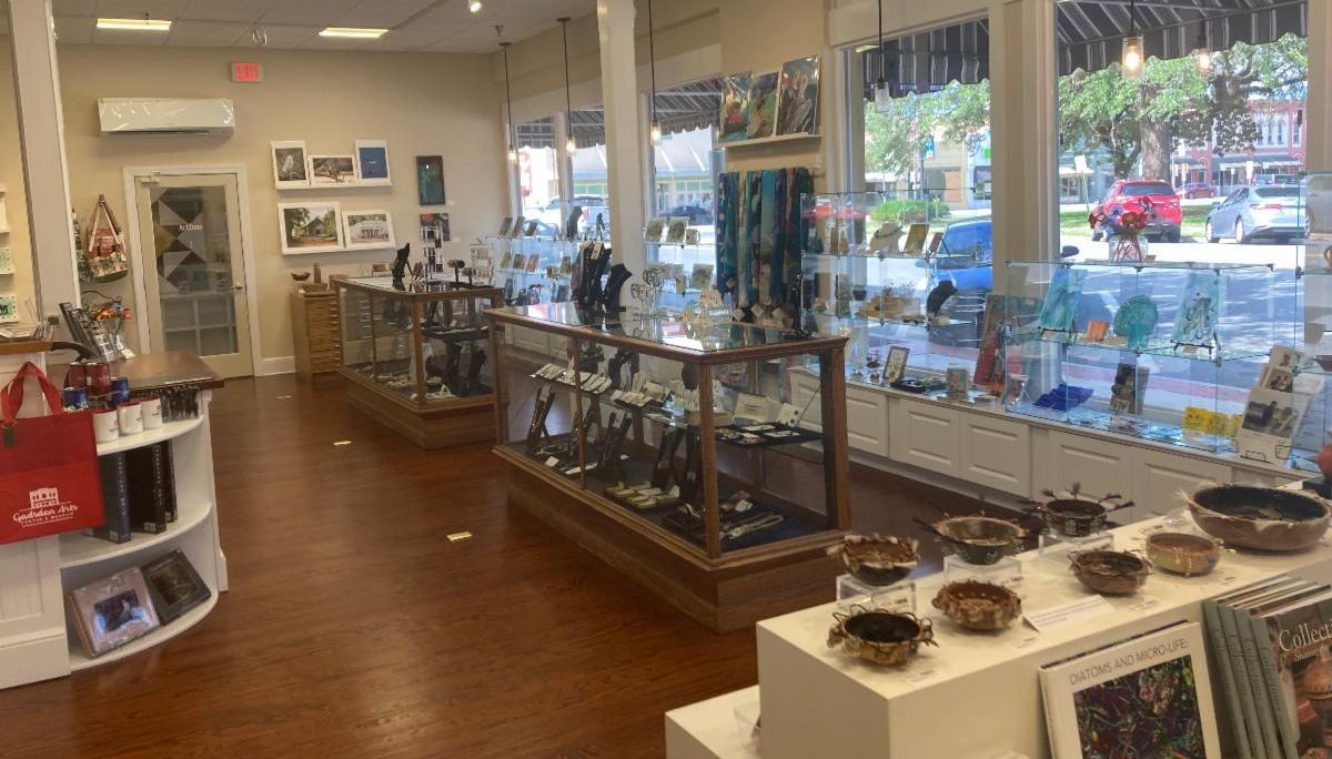 Bright jewelry shop interior with display cases, shelves, and large front windows.
