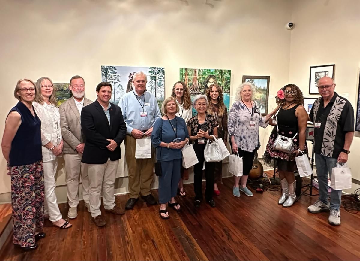 Group of people standing together at an art gallery, posing in front of framed artwork.