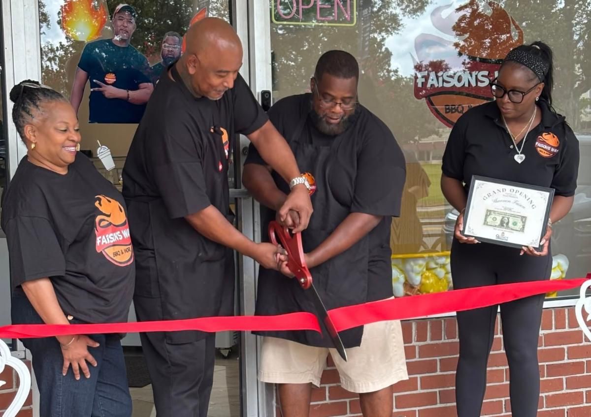 Ribbon-cutting ceremony outside storefront, with four people holding red ribbon and scissors.