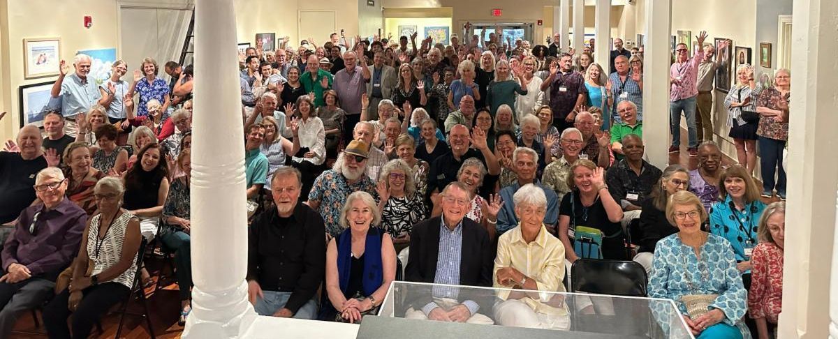 Large group gathered in a bright hall, smiling and facing the camera during a community event