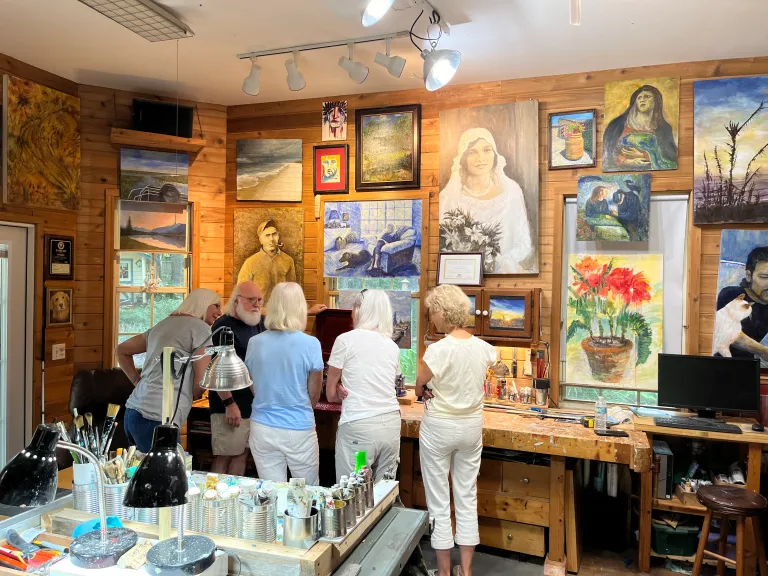 People browsing paintings in a small art gallery with colorful framed works on the walls.