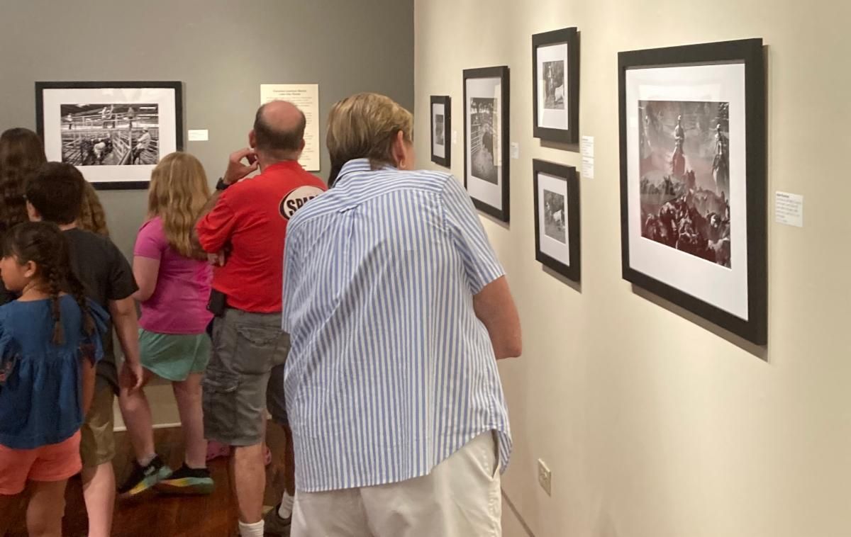 People viewing framed photographs in a gallery hallway with beige walls and wooden floor