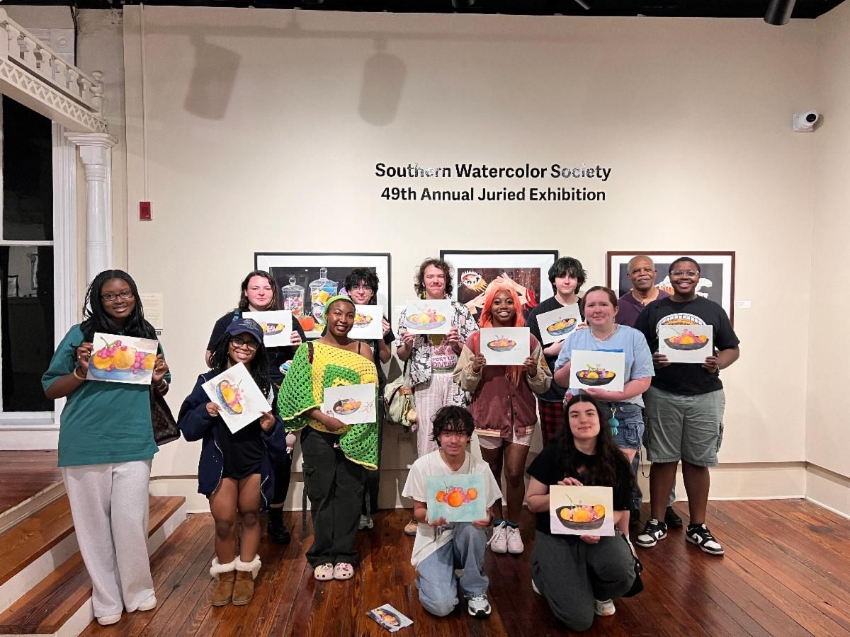 Group of people posing in a hall, holding colorful drawings and certificates in front of a wall display.