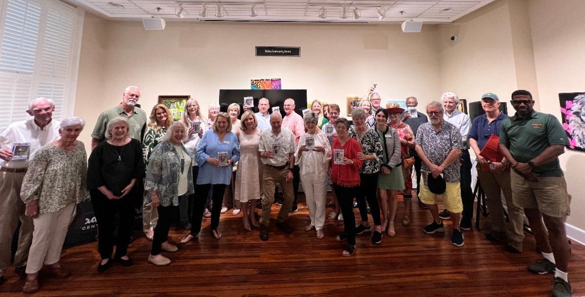 Large group posing for a photo in a banquet hall, standing on a polished wooden floor.