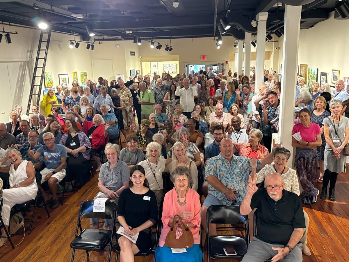 Large seated audience in a community hall, facing forward at an indoor event.