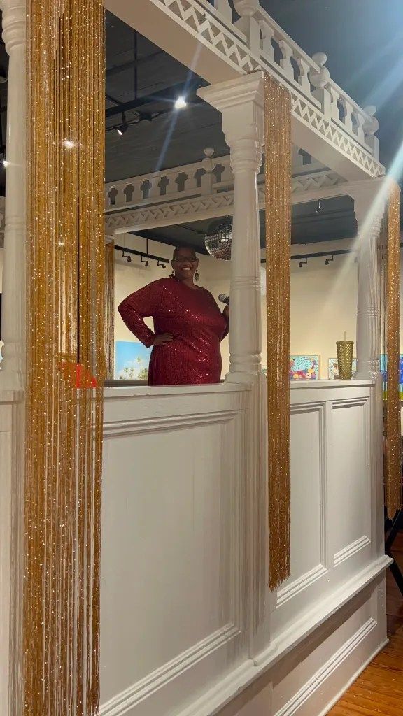 Person in a red shirt standing behind a white counter in a decorated interior with mirrored columns and warm lights