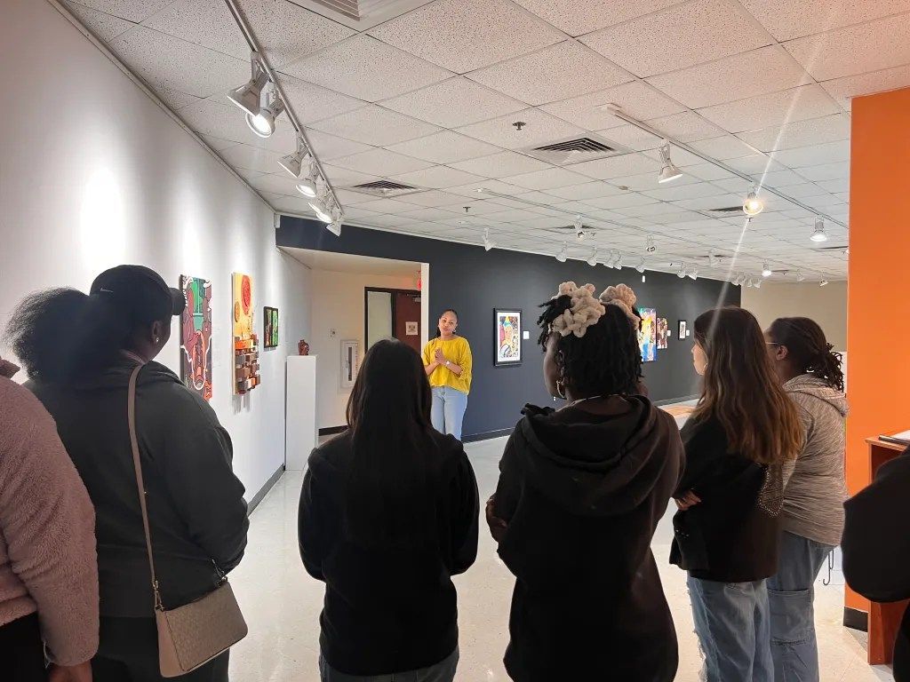 Visitors viewing colorful artwork in a gallery hallway with white walls and a tiled ceiling