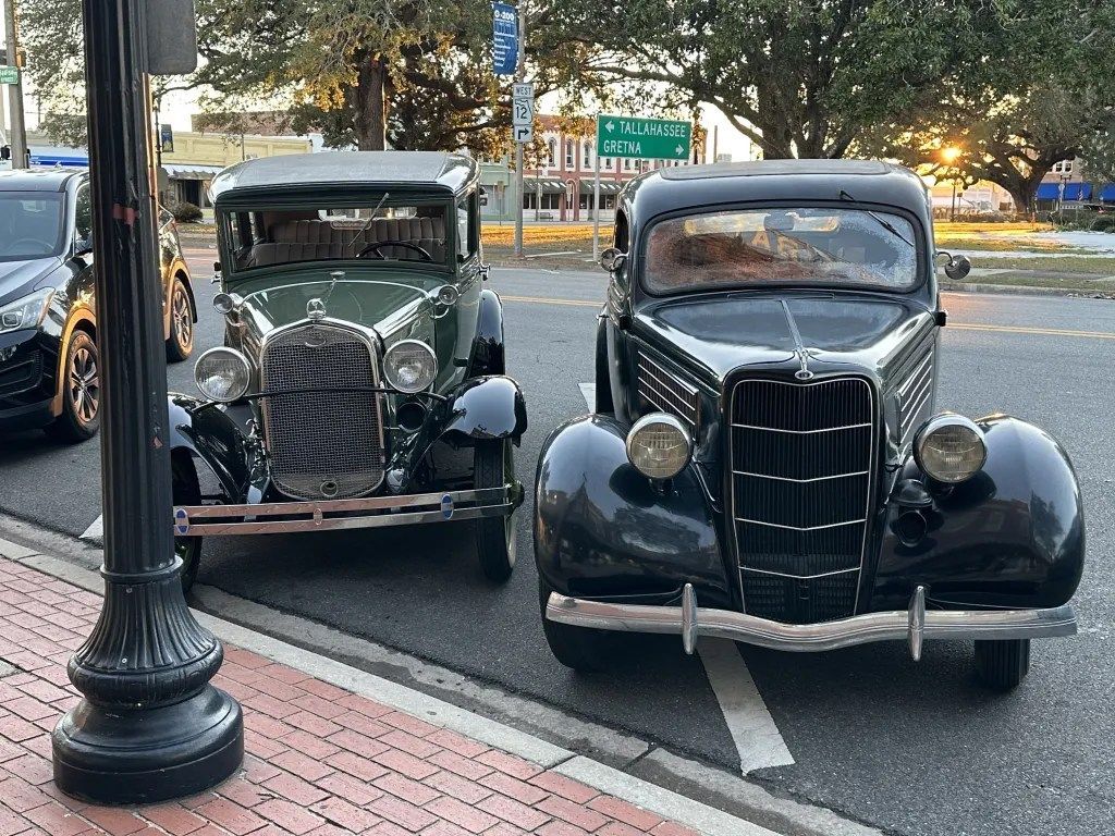 Two vintage cars parked curbside on a city street at dusk