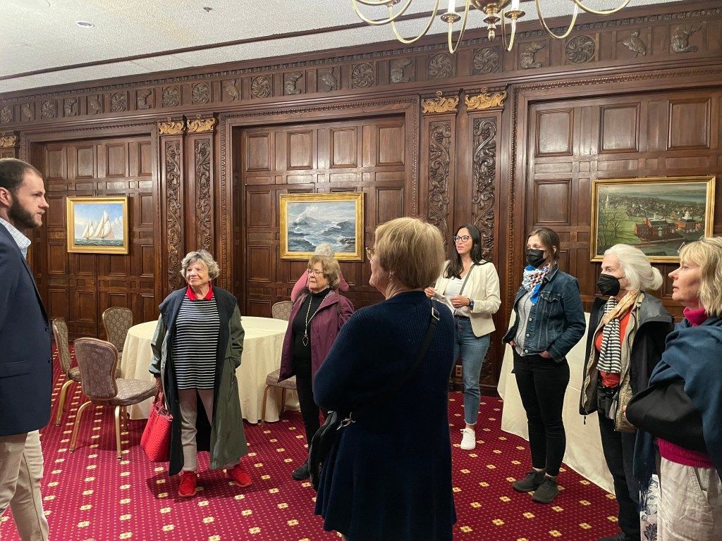 Group touring an ornate wood-paneled room with red carpet and framed paintings