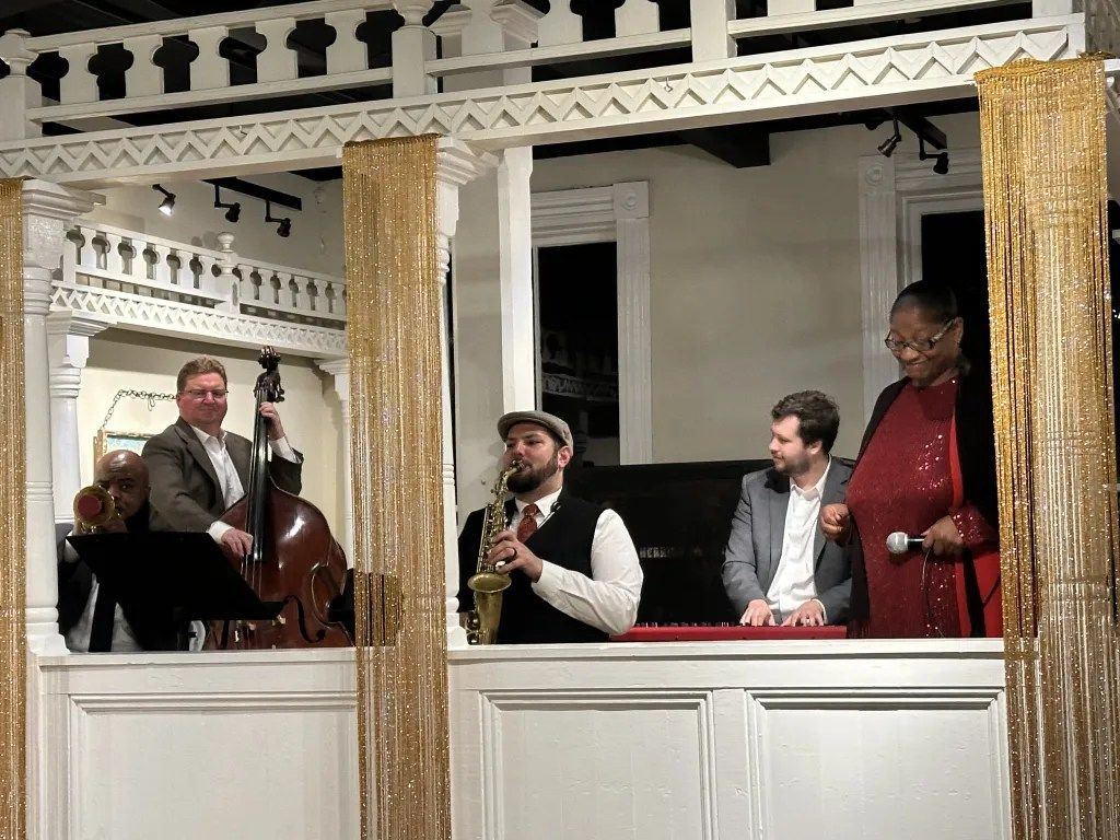 Jazz band performing on a decorated balcony with double bass, clarinet, and vocals
