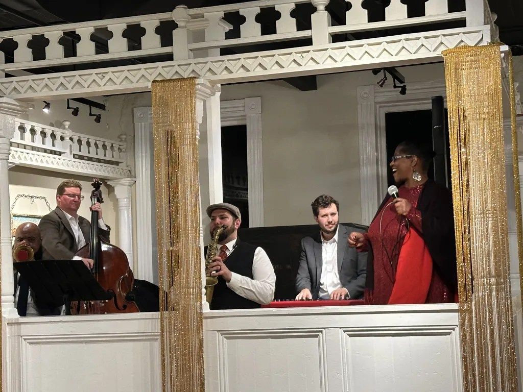 Jazz band performing on a balcony stage with gold curtains and white railings