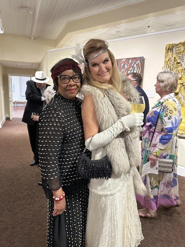 Two people posing at a formal event, one in a white gown and the other in a black polka-dot outfit.