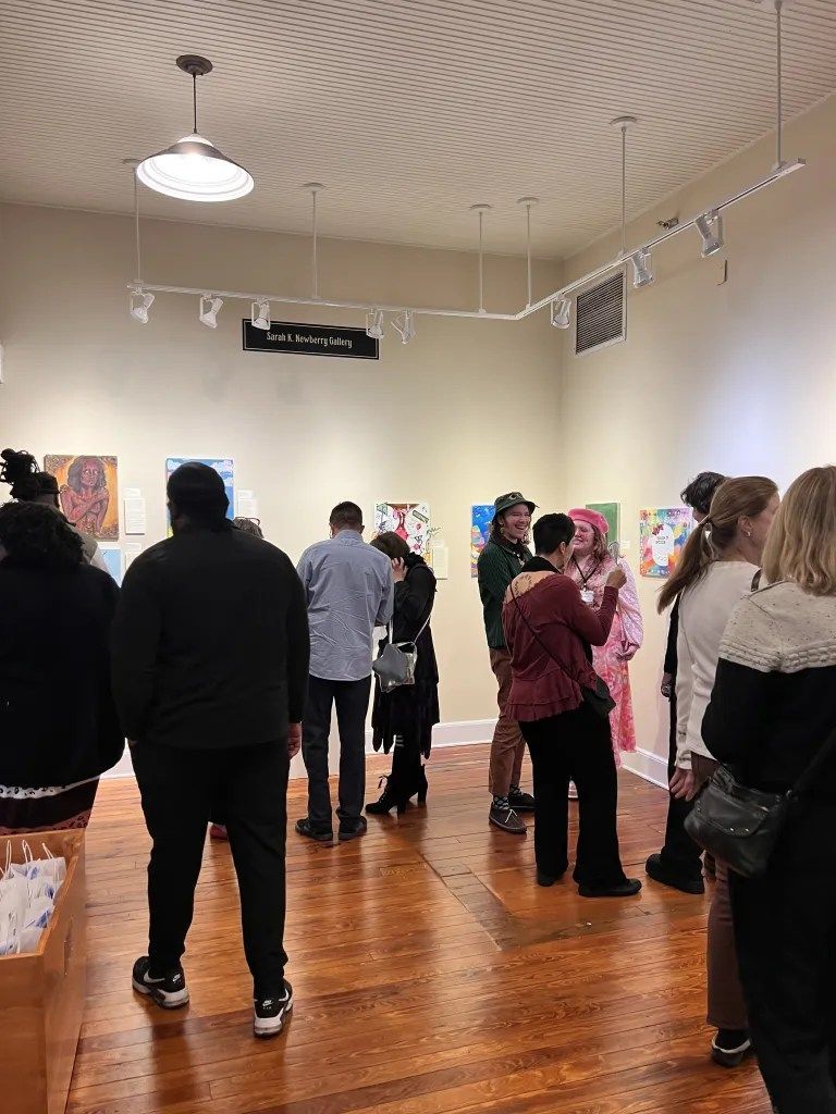 People viewing artwork in a gallery with wood floors and track lighting.