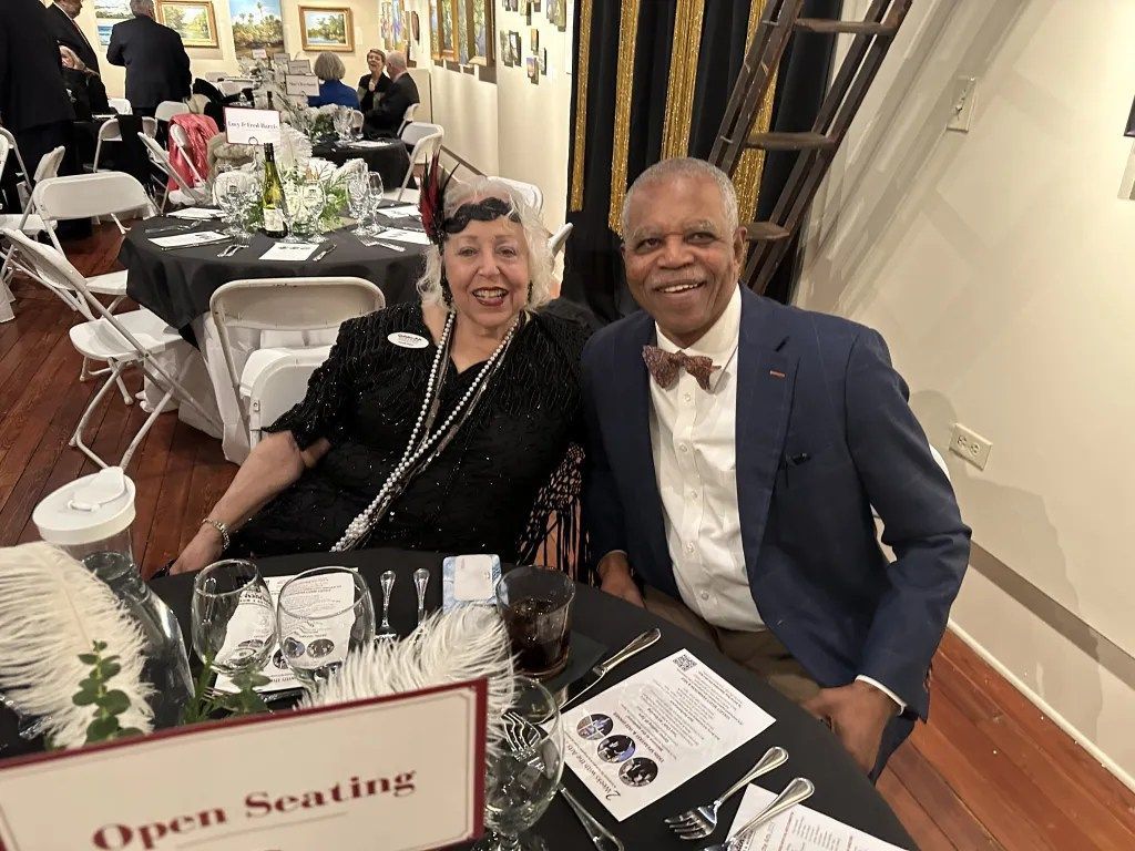Two smiling guests seated at a decorated table in a banquet hall, with an “Open Seating” sign in front.