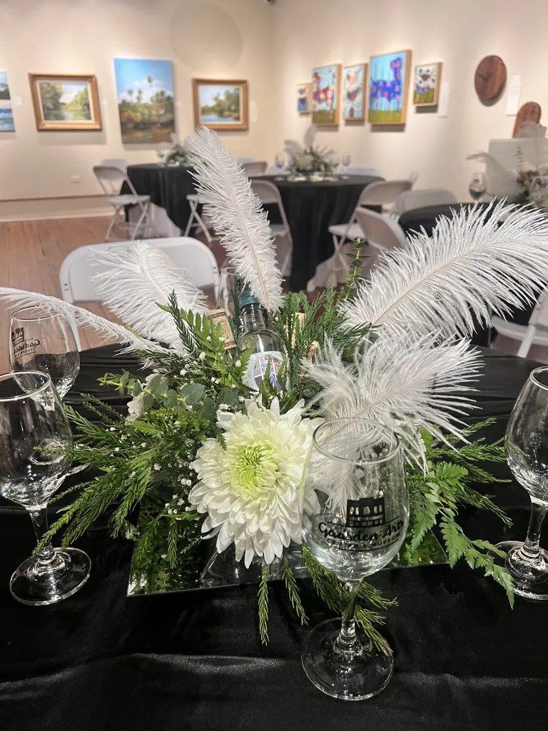 Elegant white floral centerpiece on a black tablecloth in a gallery-style event room with framed artwork on the walls