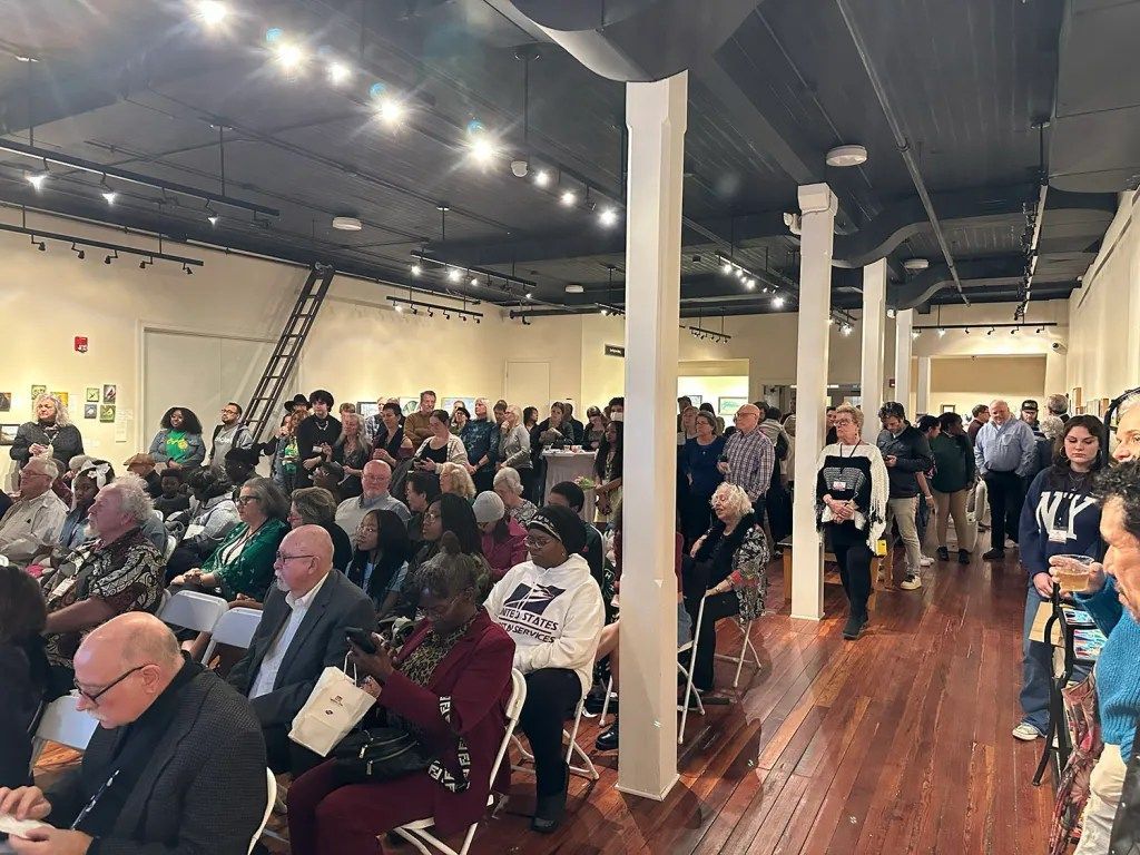 Crowded indoor event hall with seated audience and people standing along a polished wooden floor
