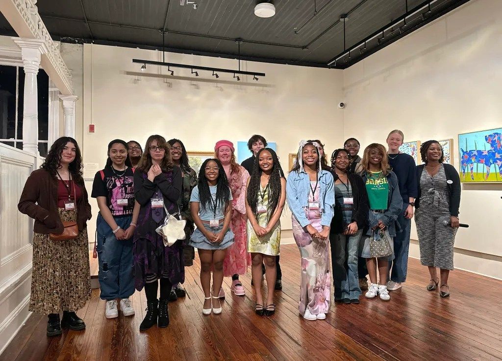 A group of people posing in an art gallery with white walls and framed artwork.
