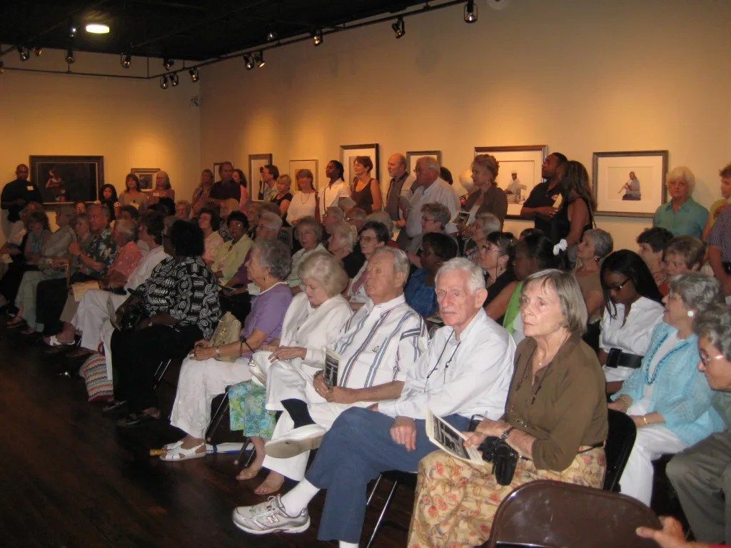 Audience seated in a gallery room watching a presentation under warm lighting