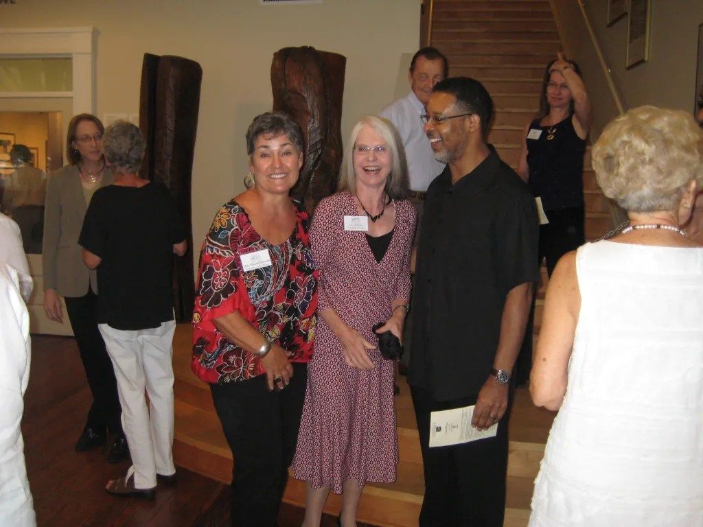 Group of people mingling at an indoor social gathering, with two women smiling in the foreground.