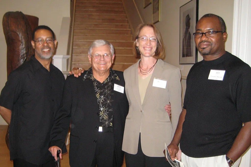 Four people standing together indoors on a staircase landing, smiling at the camera.