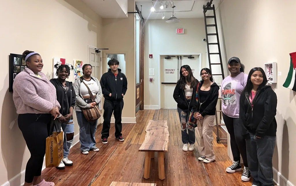 People standing in a gallery-like room beside benches, with a ladder against the back wall.