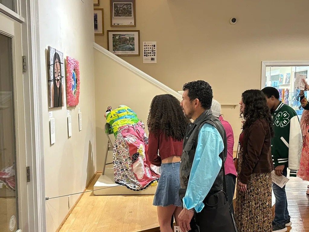People viewing colorful wall art in a gallery hallway, with a staircase and framed photos nearby
