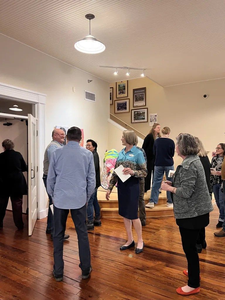 People standing in a home with hardwood floors, looking up a staircase and wall art.
