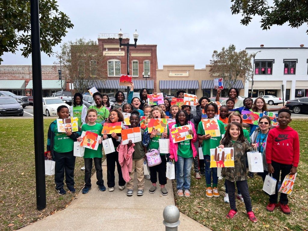 Group of people holding colorful signs in a town square, standing in front of brick buildings and a fountain.