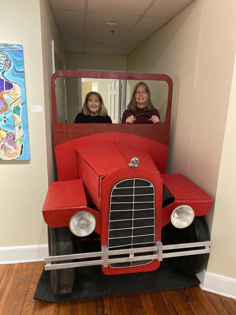 People sitting in a red vintage car cutout display in a hallway.