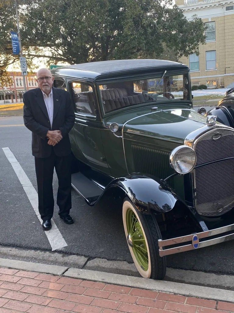 Man standing beside a vintage dark green car parked on a city street