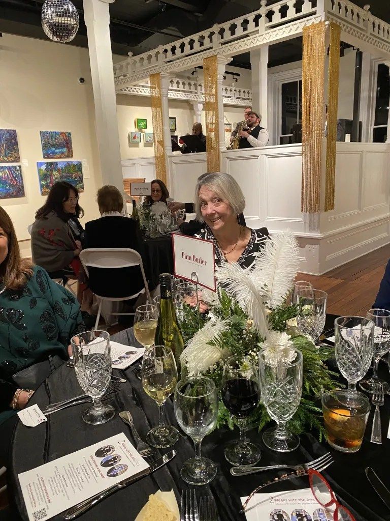 Guests seated at a candlelit dinner table in an elegant event space, with floral centerpieces and white columns.