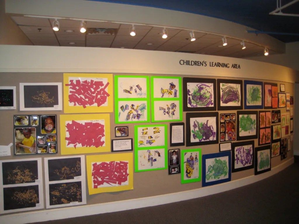Wall of colorful student art displays in a library hallway under the sign “Children’s Library Hall”