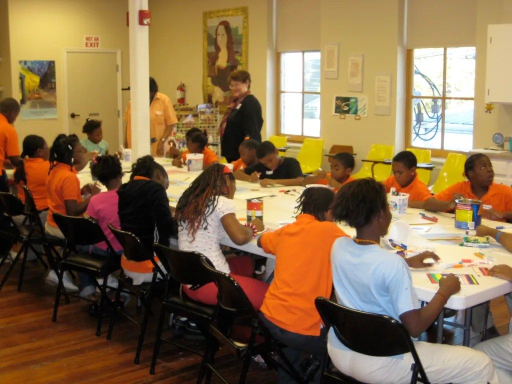 Children seated at long tables in a bright classroom, working on arts and crafts projects