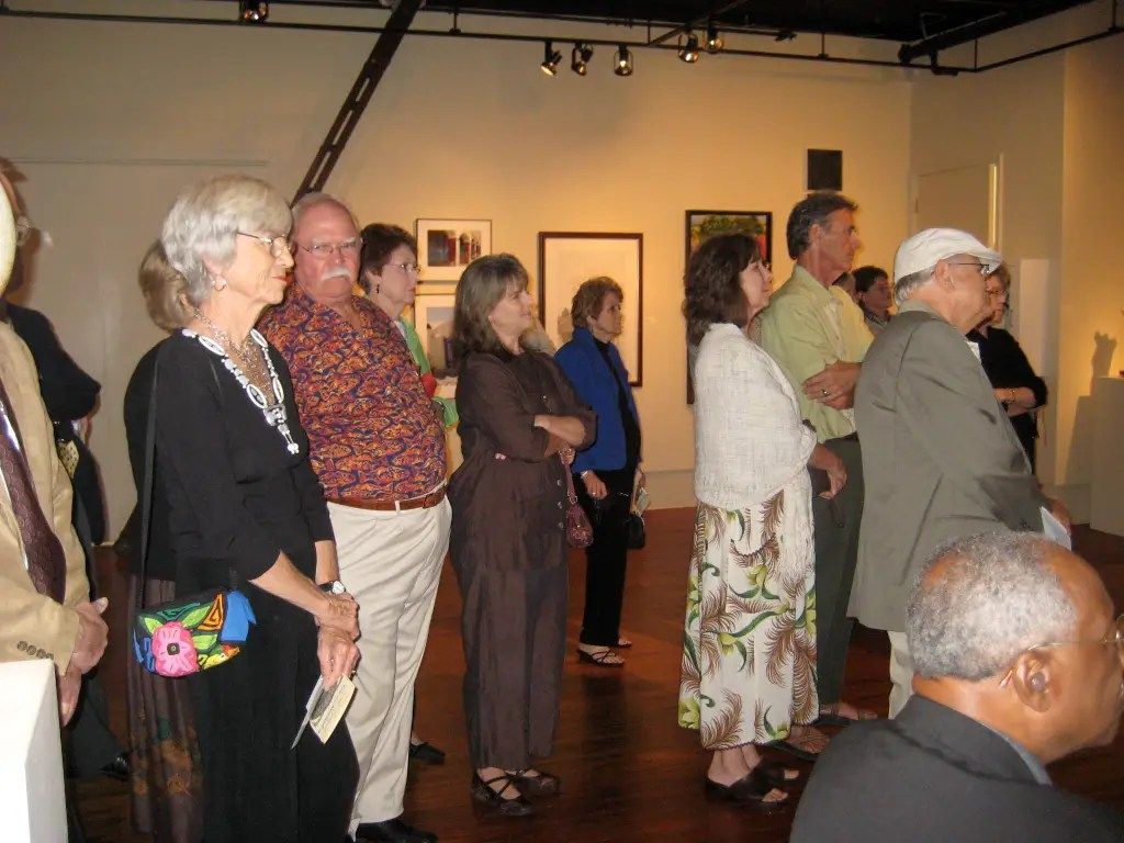 People standing in a gallery, viewing artwork on the walls and walls lit by overhead track lights