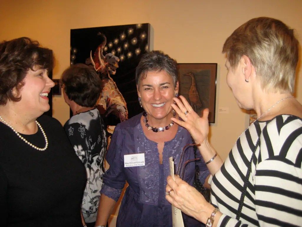 Three people chatting at an indoor social gathering, smiling and holding drinks.